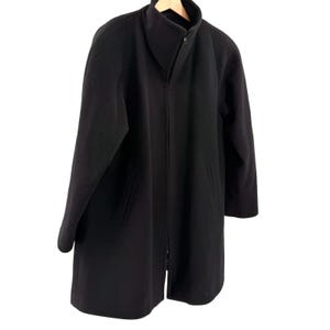 May include: A solid black coat featuring a high stand-up collar, long sleeves, and a full-length front zipper closure. The garment includes two vertical slit pockets on the front and is constructed from a smooth, uniform fabric throughout.