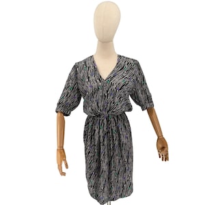 May include: A black and white patterned dress with a V-neck and short sleeves. The dress features a waist tie and is adorned with small purple and green accents. The dress is displayed on a mannequin.
