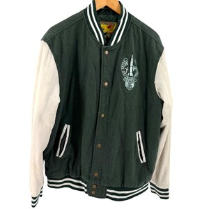 May include: A dark green varsity jacket with off-white sleeves, featuring a front button closure, striped ribbed collar, cuffs, and hem. An embroidered patch on the chest displays a rocket graphic with the text Ad Astra Miami Central HS.