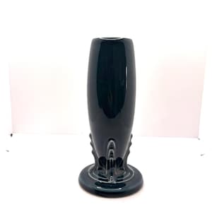 May include: A dark teal ceramic vase with a rounded body and a flared base. The vase has a glossy finish and decorative vertical ridges near the base. The vase is a decorative home decor item.