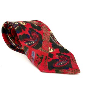 Peut inclure: Une cravate avec un fond rouge vif ornée d'un motif complexe de cachemires noirs, bleu foncé et dorés. Le tissu présente une texture lisse et est replié sur lui-même, révélant la pointe ainsi que le motif répétitif et détaillé.