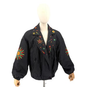May include: A black jacket featuring long sleeves, a wide collar, and a front zipper closure. The garment is decorated with colorful embroidered celestial motifs, including suns and stars in shades of yellow, orange, red, and green.