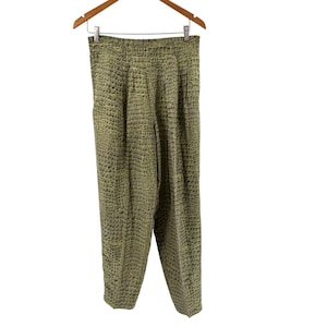Puede incluir: Pantalones de talle alto con un patrón texturizado en relieve de piel de cocodrilo en tonos verde oliva y chartreuse. Estos pantalones tienen una silueta de pierna cónica con pliegues frontales sutiles y una cintura estructurada, colgados de una percha.