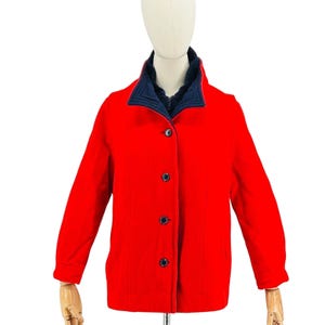 May include: A bright red jacket with a navy blue collar and lining. The jacket has a button-up front with four dark buttons. The sleeves are long, and the jacket appears to be made of a wool or wool-blend material. The jacket is displayed on a mannequin.