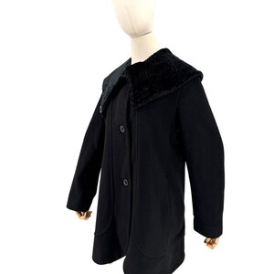 May include: A black coat featuring a large, textured faux fur collar and a front button closure. The garment has long sleeves and two vertical seam details running down the front, extending into rounded pocket-like shapes at the hemline.