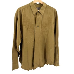 May include: A long-sleeved button-down shirt in a solid olive green color. The shirt features a pointed collar and a decorative vertical panel on each side of the chest, consisting of intricate, tonal geometric stitching and pleat details.