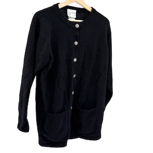 May include: A black long-sleeve cardigan sweater featuring a crew neckline, a front button closure with six round silver-toned buttons, and two patch pockets at the bottom. The interior neck label displays the brand name Laura Ashley.