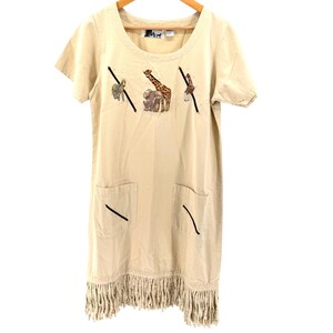 May include: A beige short-sleeved dress featuring a round neckline and a fringe hem. The front is decorated with embroidered animal figures including a zebra, an elephant, and a giraffe, along with two front pockets accented by black diagonal lines.