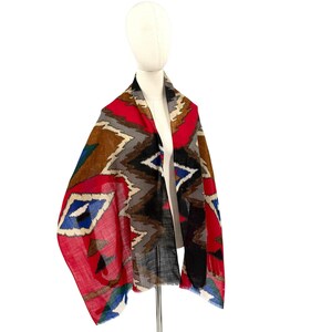 Peut inclure: Une écharpe légère présentant un motif géométrique vibrant dans des tons de rouge, marron, gris, noir et bleu. Le design se compose de formes répétitives en losange et en zigzag sur le tissu, créant un effet visuel audacieux et coloré.