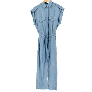 May include: A light blue jumpsuit featuring a collared neckline, short cap sleeves, and shoulder epaulets. The garment includes two chest pockets with flaps, a button-down front closure, and a drawstring waist with a tie belt for a cinched fit.