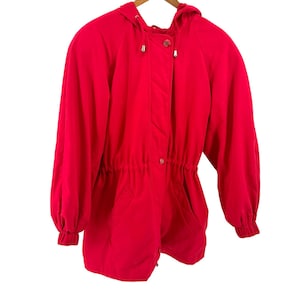 May include: A bright red hooded jacket featuring long sleeves with elasticized cuffs, a drawstring hood with silver-toned metal toggles, and a front placket with visible buttons. The waist is cinched with an internal drawstring detail.