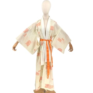 May include: Cream-colored kimono with a floral pattern in coral. The kimono features wide sleeves and an orange sash tied at the waist. The garment is displayed on a mannequin.