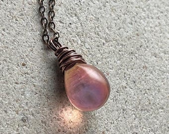 May include: A teardrop-shaped pendant with a pearlescent pink and purple finish, suspended from a dark copper-toned metal chain. The top of the pendant is secured with a decorative wire-wrapped copper coil that connects directly to the chain links.