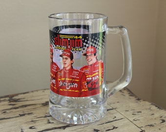 Könnte beinhalten: Ein Bierkrug aus klarem Glas mit einer Slim Jim Racing Team-Grafik, der Nummer 44, einem Zielflaggenmuster und Illustrationen von Rennfahrern in roten Uniformen. Das Design enthält das Slim Jim-Logo und schwarze, aufgedruckte Unterschriften.