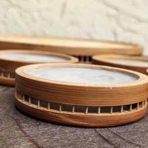 K&ouml;nnte beinhalten: Eine Sammlung runder Holzuntersetzer mit einer hellen, glatten Oberfl&auml;che. Die Untersetzer bestehen aus d&uuml;nnem, geschichtetem Holz und haben ein dekoratives, geschlitztes Design an den Seiten. Im Hintergrund befindet sich ein gr&ouml;&szlig;erer, &auml;hnlicher Holztablett.