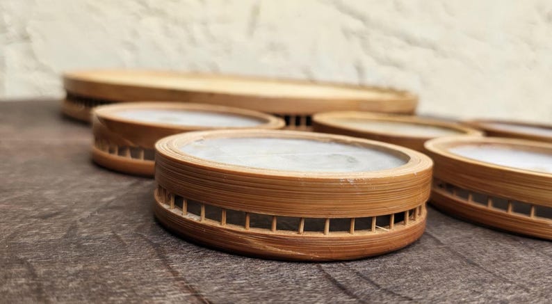 K&ouml;nnte beinhalten: Eine Sammlung runder Holzuntersetzer mit einer hellen, glatten Oberfl&auml;che. Die Untersetzer bestehen aus d&uuml;nnem, geschichtetem Holz und haben ein dekoratives, geschlitztes Design an den Seiten. Im Hintergrund befindet sich ein gr&ouml;&szlig;erer, &auml;hnlicher Holztablett.