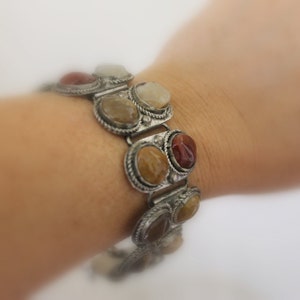 May include: A silver bracelet with a chain link design and oval-shaped stones in shades of brown, red, and white.