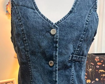 May include: A blue acid-wash denim vest featuring a V-neckline, a front button closure with three silver-toned metal buttons, and a single horizontal welt pocket on the left side. The garment has visible vertical seam detailing along the front.