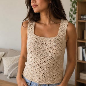 May include: A beige sleeveless crochet tank top featuring a repeating fan-shaped stitch pattern, a square neckline, and wide shoulder straps. The garment is constructed with a delicate openwork design and is paired with light blue denim jeans.