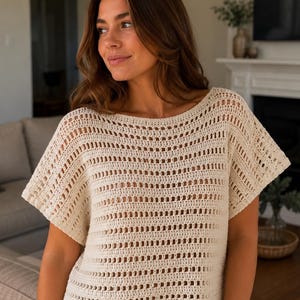May include: A cream-colored crochet top featuring a wide boat neckline and short, loose sleeves. The garment is constructed with alternating rows of solid double crochet stitches and openwork mesh patterns, creating a textured, semi-sheer appearance.