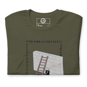 Könnte beinhalten: Olivgrünes T-Shirt mit einer Cartoon-Illustration einer Backsteinmauer mit einer Holzleiter und einer schwarzen Katze. Auf der Mauer steht das Wort "CREEPY". Das Shirt hat ein Etikett mit der Aufschrift "XS Nicaragua".