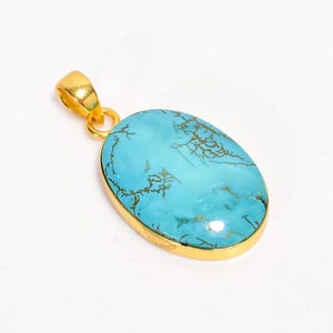 May include: A gold-colored pendant with an oval, turquoise-colored stone. The stone has brown veining and is set in a gold-colored bezel. The pendant has a gold-colored bail for attaching to a chain.
