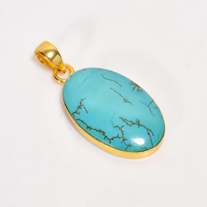 Puede incluir: Colgante dorado con una piedra ovalada de color turquesa con vetas marrones. La piedra está engastada en un bisel dorado, y el colgante tiene una fianza dorada para una cadena. Joyería.