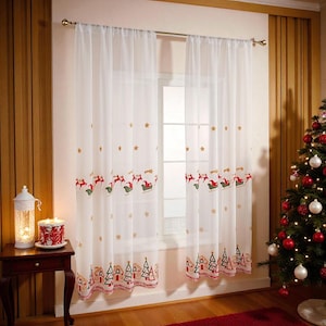 May include: Sheer white Christmas curtains with embroidered reindeer pulling sleighs, stars, and village scenes. The curtains hang in front of a window, with a Christmas tree and red rug visible in the background.