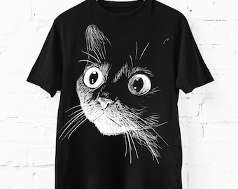 Può includere: Una t-shirt nera a maniche corte con un disegno a linee bianche raffigurante un muso di gatto con occhi grandi e spalancati e baffi dettagliati. Il design è centrato sul petto e mostra un'illustrazione in stile schizzo della testa del felino.