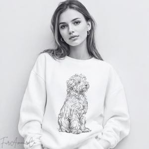 Może przedstawiać: Biała bluza z czarno-białą ilustracją psa. Pies jest przedstawiony w pozycji siedzącej, z szczeg&oacute;łowymi liniami definiującymi jego sierść. Projekt bluzy skupia się na ilustracji psa.