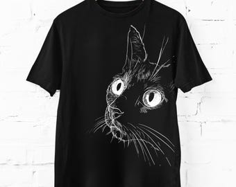 Può includere: Una t-shirt nera a maniche corte con un'illustrazione a linee bianche del muso di un gatto sul davanti. Il disegno raffigura la testa del gatto di profilo con occhi grandi e dettagliati e baffi prominenti, in uno stile grafico a schizzo.