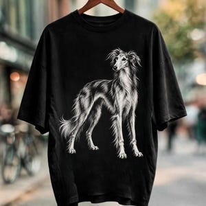 Op de afbeelding: Een zwart t-shirt met korte mouwen voorzien van een gedetailleerde witte lijntekening van een langharige Borzoi-hond in profiel. De afbeelding is gecentreerd op de borst en toont het slanke postuur, de vloeiende vacht en de elegante kenmerken.