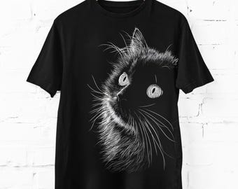 May include: A black short-sleeve t-shirt featuring a white line art graphic of a cat's face. The illustration highlights the cat's eyes, whiskers, and fur texture in fine white strokes against the dark fabric, centered on the front of the shirt.