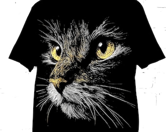 May include: A black short-sleeve t-shirt featuring a detailed graphic print of a cat face. The cat is rendered in white and gold line art, highlighting its piercing yellow eyes, textured fur, and long whiskers against the solid black fabric.