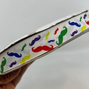 Könnte beinhalten: Ein weißes Band mit einem sich wiederholenden Muster aus bunten Schnurrbärten. Die Schnurrbärte sind in verschiedenen Farben, darunter Rot, Gelb, Grün, Blau und Lila.