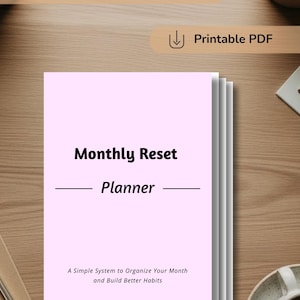 May include: A stack of pink paper with the words "Monthly Reset Planner" printed in black. The text "A Simple System to Organize Your Month and Build Better Habits" is below. The words "Undated Monthly Reset Planner" and "Printable PDF" are also visible.
