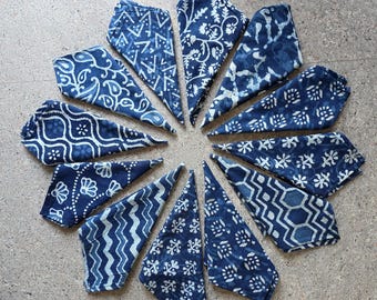 Puede incluir: Un conjunto de servilletas de tela azul índigo dispuestas en círculo. Cada servilleta presenta un patrón blanco único, incluyendo diseños florales, geométricos y abstractos. Las servilletas son de tela suave.