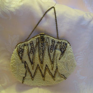 May include: A vintage beaded evening bag with a gold chain strap. The bag is made of white beads and has a geometric pattern with gold accents.