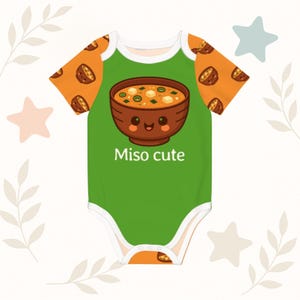 May include: A green baby onesie with orange sleeves featuring a cartoon miso soup bowl with a smiling face. The text "Miso cute" is below the bowl. The sleeves have a repeating pattern of miso soup bowls.