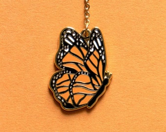 May include: A gold chain with a monarch butterfly charm. The butterfly is orange with black markings and has a gold outline.