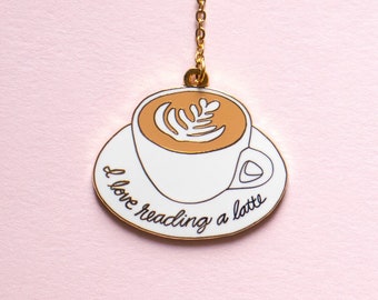 May include: A white enamel charm with a gold chain, depicting a cup of latte with the text "I love reading a latte".