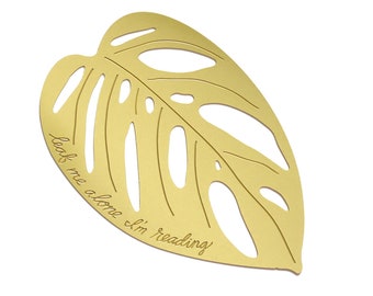 May include: Gold-colored metal bookmark shaped like a monstera leaf with the text "Leave me alone I'm reading" engraved on it.