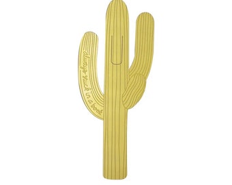 May include: A gold-colored metal bookmark shaped like a cactus with the text "always stuck in a book" on one of the arms.