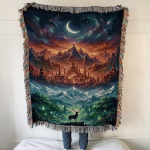 Könnte beinhalten: Eine gewebte Decke mit einer Fantasy-Landschaft, die ein Schloss, Berge und einen Halbmond zeigt. Die Decke hat einen Fransenrand und zeigt einen Hirsch in einem Wald. Die Farbpalette umfasst Blau-, Orange- und Grüntöne.