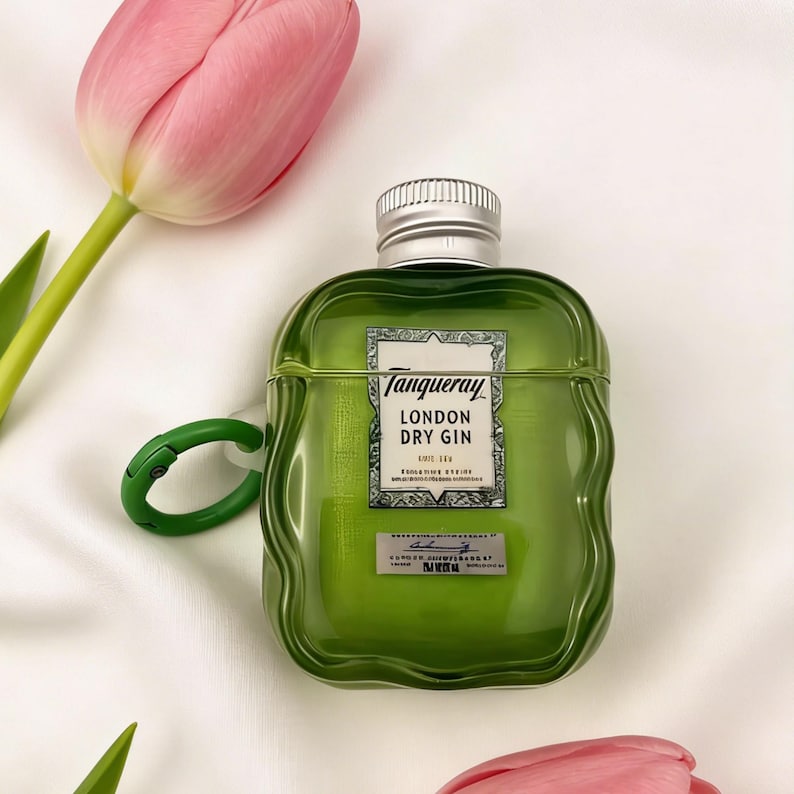 Peut inclure: Un &eacute;tui de protection vert en forme de bouteille de gin Tanqueray London Dry. Il comporte un bouchon argent&eacute; et un mousqueton vert. L'&eacute;tiquette indique "Tanqueray LONDON DRY GIN". Des tulipes roses sont en arri&egrave;re-plan.