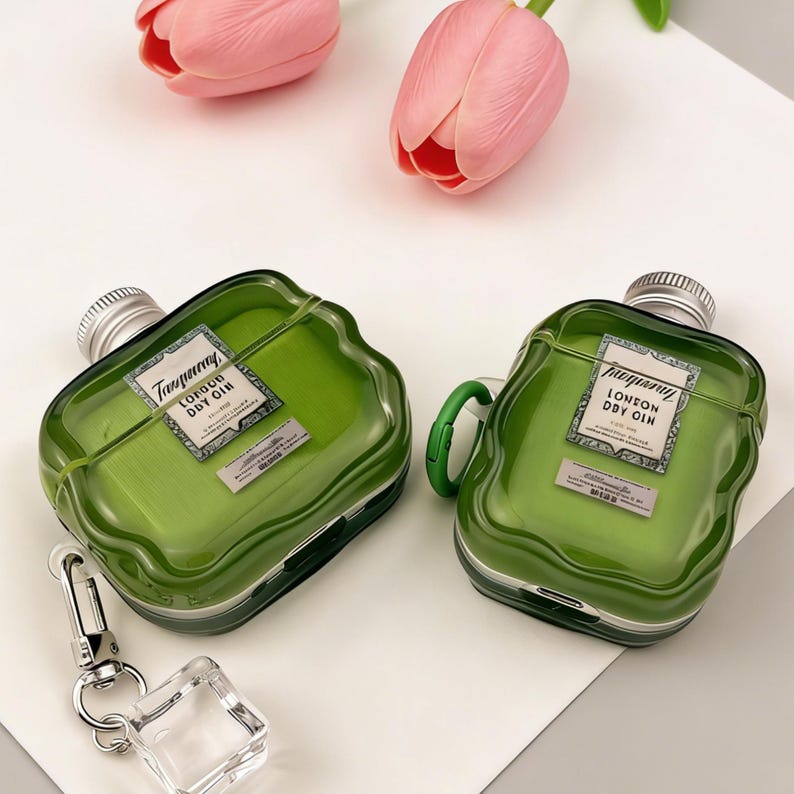 Peut inclure: Deux &eacute;tuis pour AirPod verts en forme de bouteilles de gin, avec des bouchons argent&eacute;s et des &eacute;tiquettes indiquant "London Dry Gin". L'un a une poign&eacute;e verte, l'autre un fermoir argent&eacute; avec un charm carr&eacute; transparent. Des tulipes roses sont en arri&egrave;re-plan.
