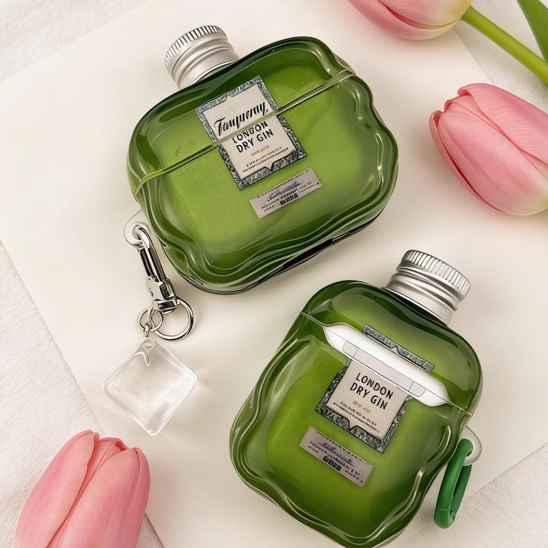 Peut inclure: Deux &eacute;tuis pour AirPod verts en forme de bouteille, avec des bouchons argent&eacute;s et l'inscription "Tanqueray London Dry Gin". L'un d'eux est muni d'un clip argent&eacute; et d'un charm carr&eacute; transparent. Des tulipes roses en arri&egrave;re-plan.