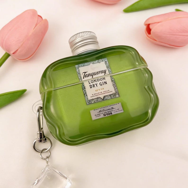 Peut inclure: Un &eacute;tui vert en forme de bouteille pour &eacute;couteurs sans fil, ressemblant &agrave; une bouteille de Tanqueray London Dry Gin. L'&eacute;tui a un bouchon argent&eacute; et un mousqueton argent&eacute;. L'&eacute;tiquette indique "Tanqueray London Dry Gin". Des tulipes roses sont en arri&egrave;re-plan.