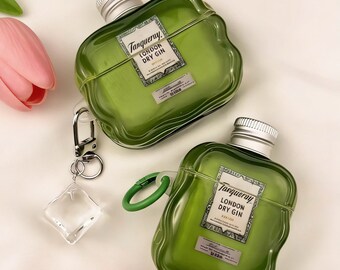 May include: Two green, bottle-shaped AirPod cases with silver tops and the "Tanqueray London Dry Gin" label. One case has a green loop and the other has a silver carabiner with a clear charm. Pink and green flowers are in the background.