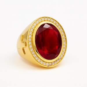 Könnte beinhalten: Ein goldfarbener Ring mit einem großen, oval geschliffenen, tiefroten Edelstein. Der Edelstein ist von kleinen, klaren Steinen umgeben. Der Ring hat ein dickes Band mit einem Kreuzdesign an der Seite.